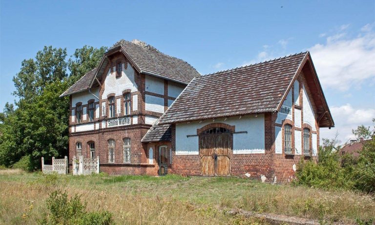 Derelict rural train station in Smolno Wielkie, Poland, featuring overgrown tracks and a crumbling station building.